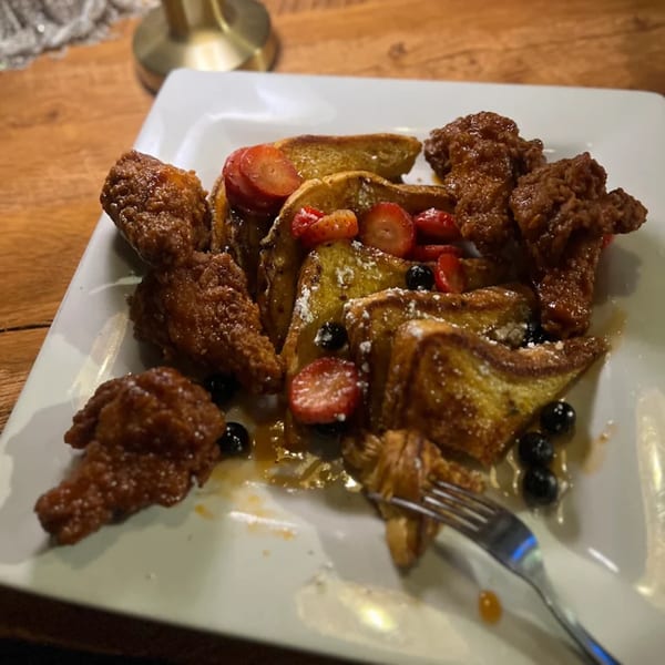 Flight Social's chicken and waffles with strawberries, blueberries, and powdered sugar on a white plate.